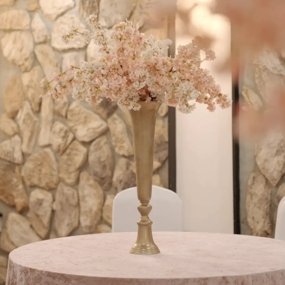 Ein goldene Vase mit rosa und weißen Blumen steht auf einem runden Tisch vor Steinwand